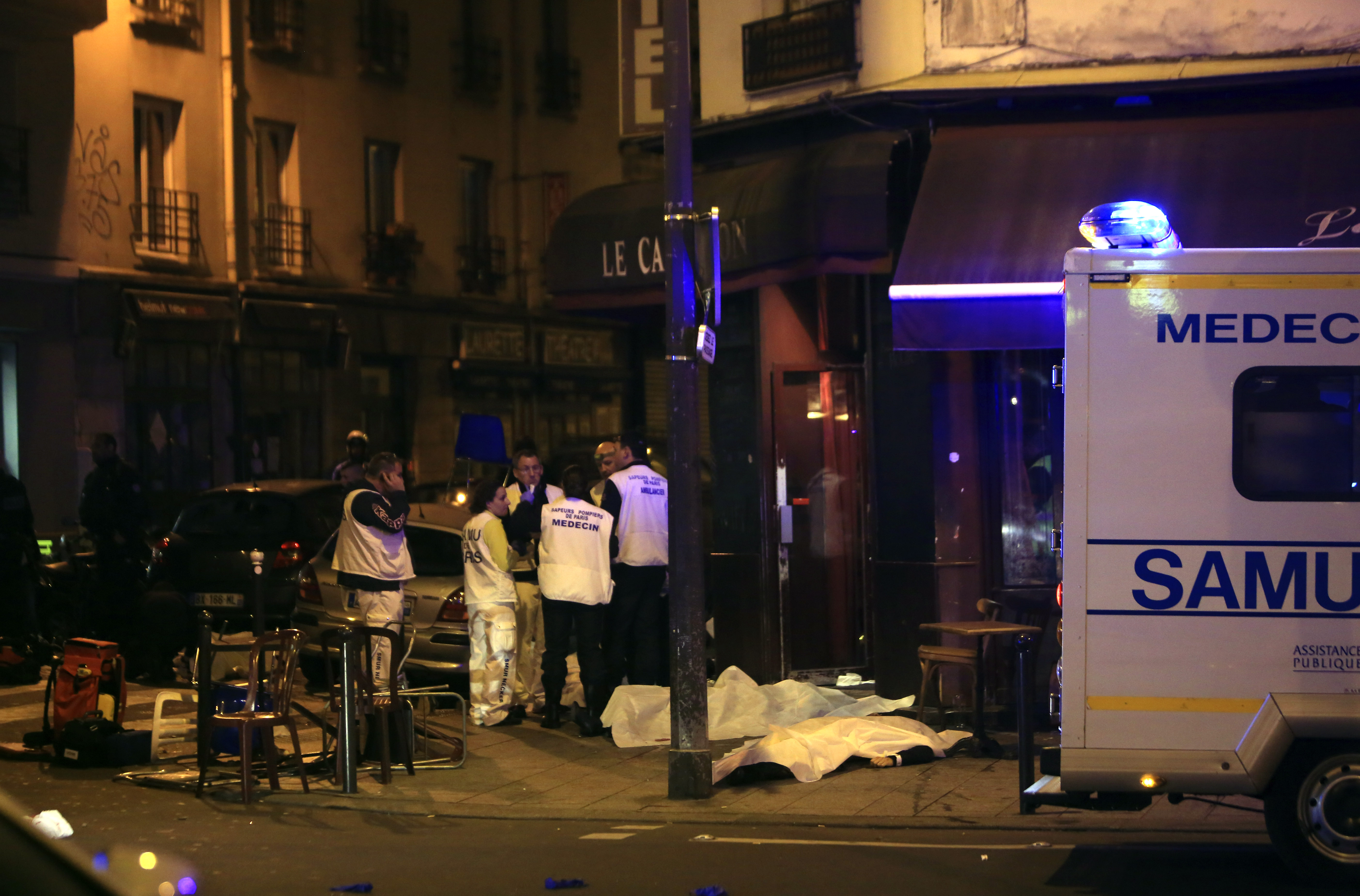 Medics stand by victims in a Paris restaurant, Friday, Nov. 13, 2015. Police officials in France on Friday reported a shootout in a Paris restaurant and an explosion in a bar near a Paris stadium. It was unclear if the events were linked. (AP Photo/Thibault Camus)